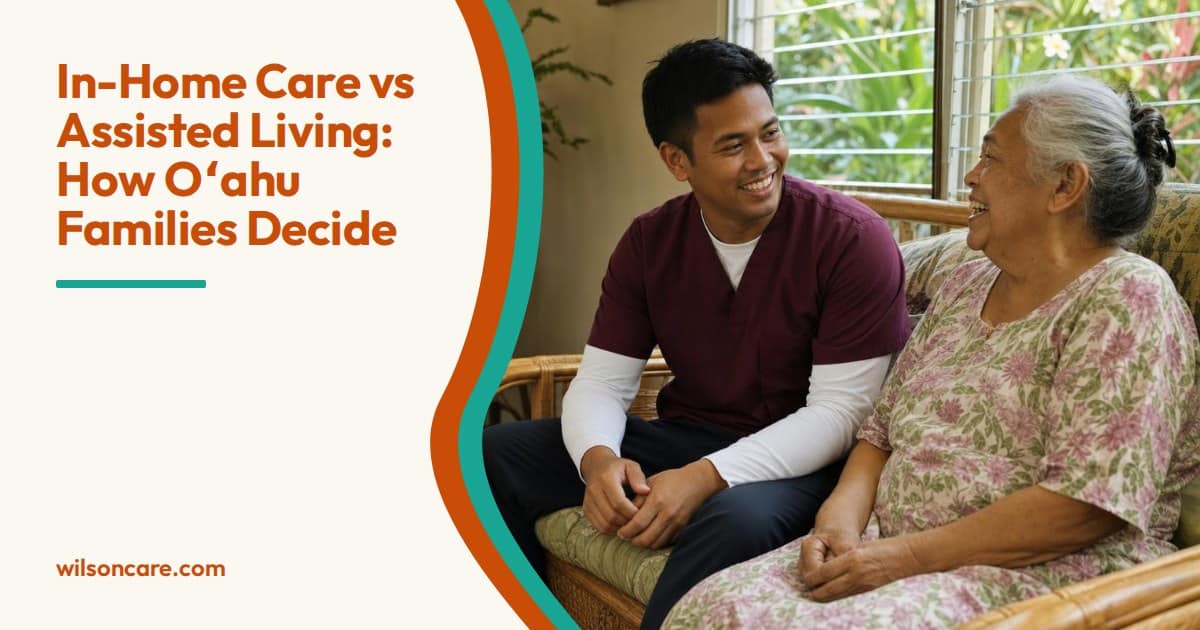 A caregiver in a burgundy top and an older woman in a floral dress laugh together on a rattan sofa in her sunlit living room